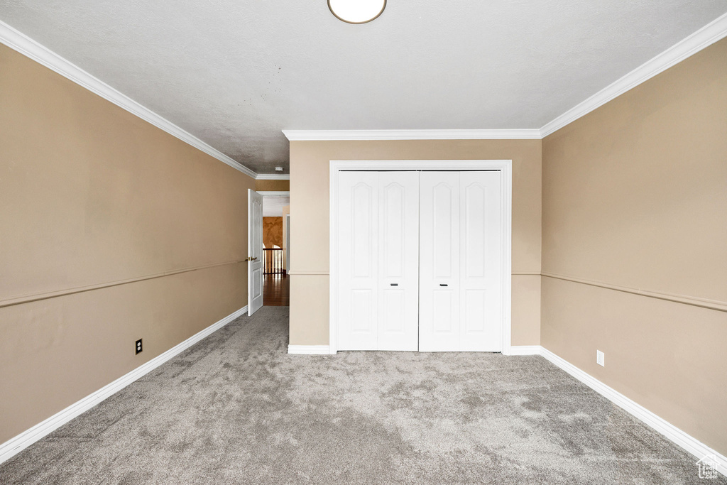 Unfurnished bedroom featuring ornamental molding, a closet, carpet, and baseboards
