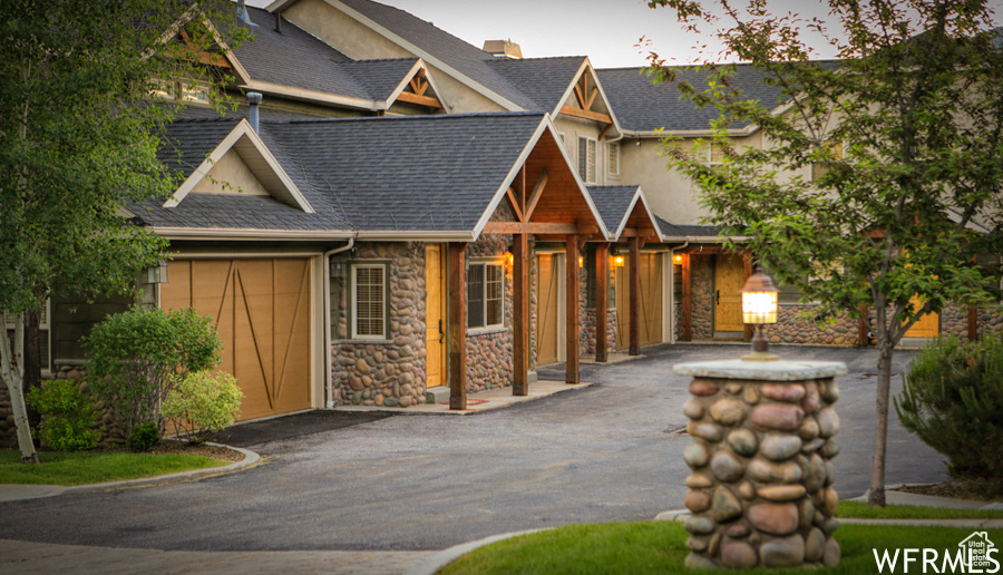 View of front facade featuring roof with shingles, stucco siding, and stone siding