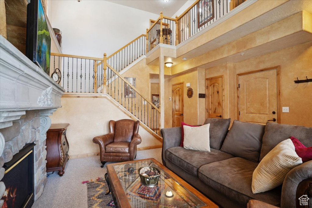 Carpeted living room featuring a fireplace, stairway, and a high ceiling