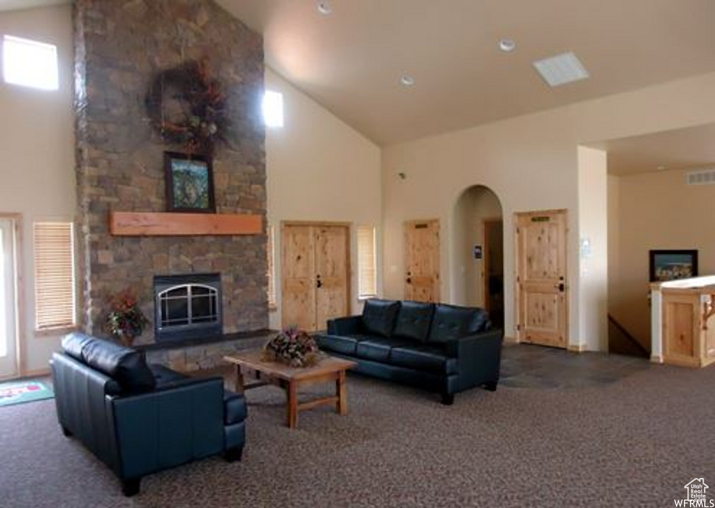 Living room with high vaulted ceiling, arched walkways, carpet floors, and a stone fireplace