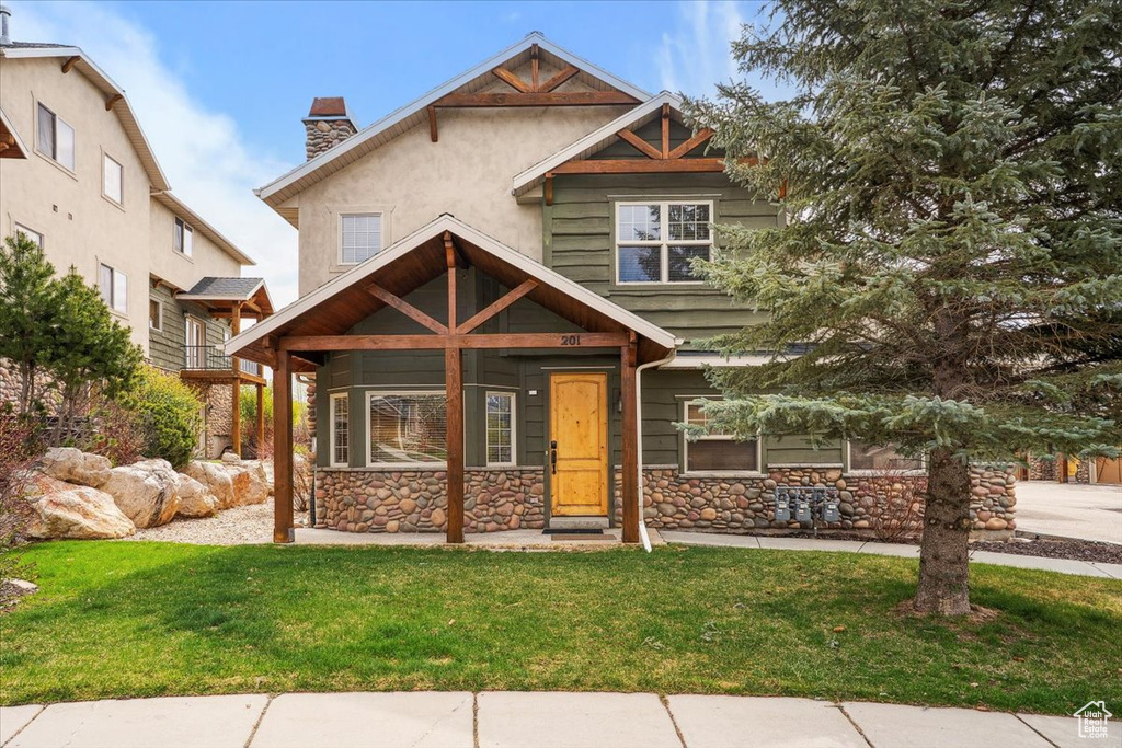 Craftsman house featuring stucco siding, a chimney, a front yard, and stone siding