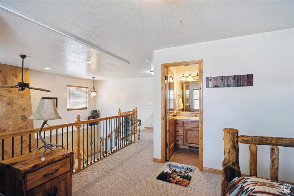 Hall featuring a sink, an upstairs landing, baseboards, a textured ceiling, and light colored carpet