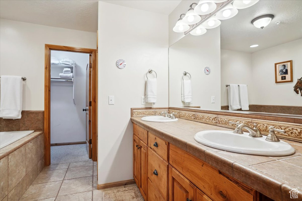 Bathroom featuring a walk in closet, tile patterned flooring, double vanity, and a sink