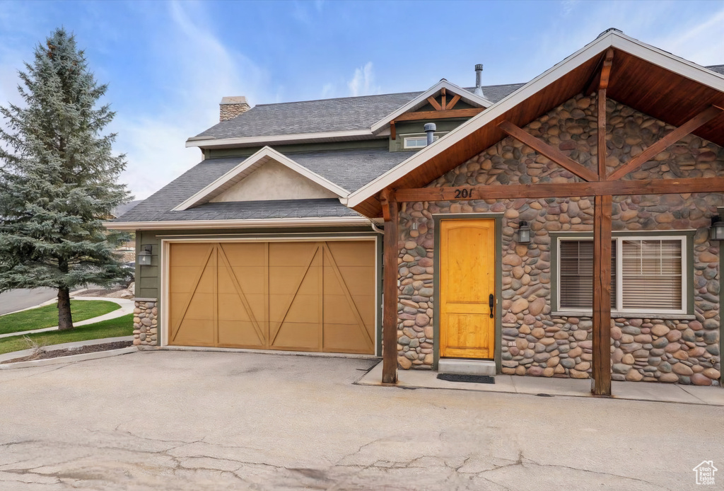 Craftsman house with a chimney, stone siding, an attached garage, and aphalt driveway