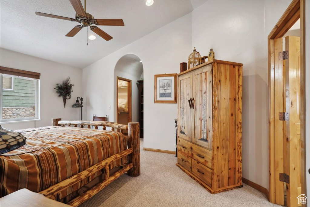 Bedroom with baseboards, arched walkways, vaulted ceiling, light carpet, and a ceiling fan
