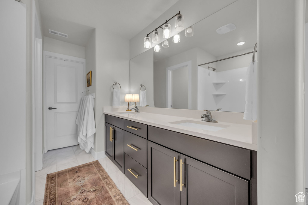 Full bath with a sink, double vanity, visible vents, marble finish floor, and a shower