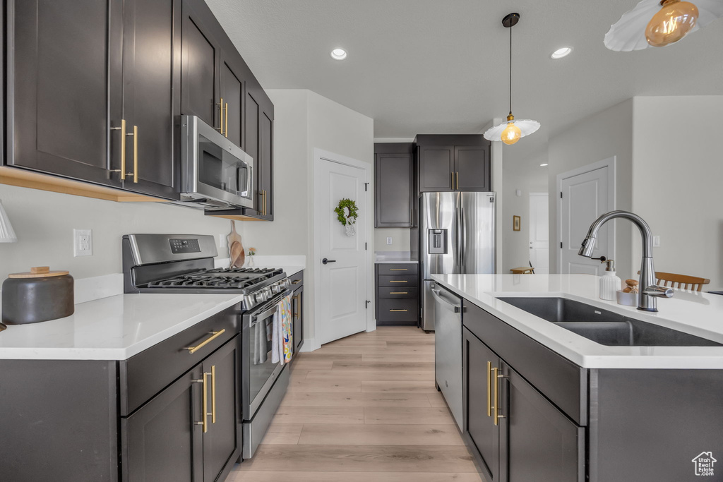 Kitchen featuring light wood finished floors, a sink, pendant lighting, light countertops, and appliances with stainless steel finishes