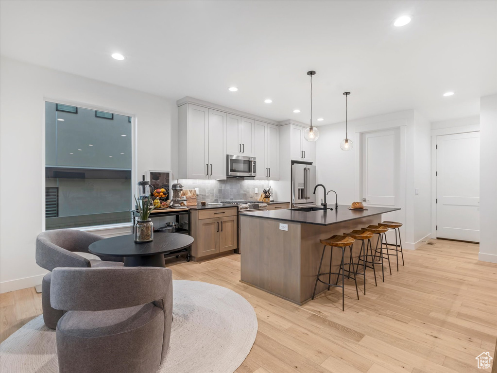 Kitchen with high end appliances, a breakfast bar area, light wood-style flooring, backsplash, and dark countertops
