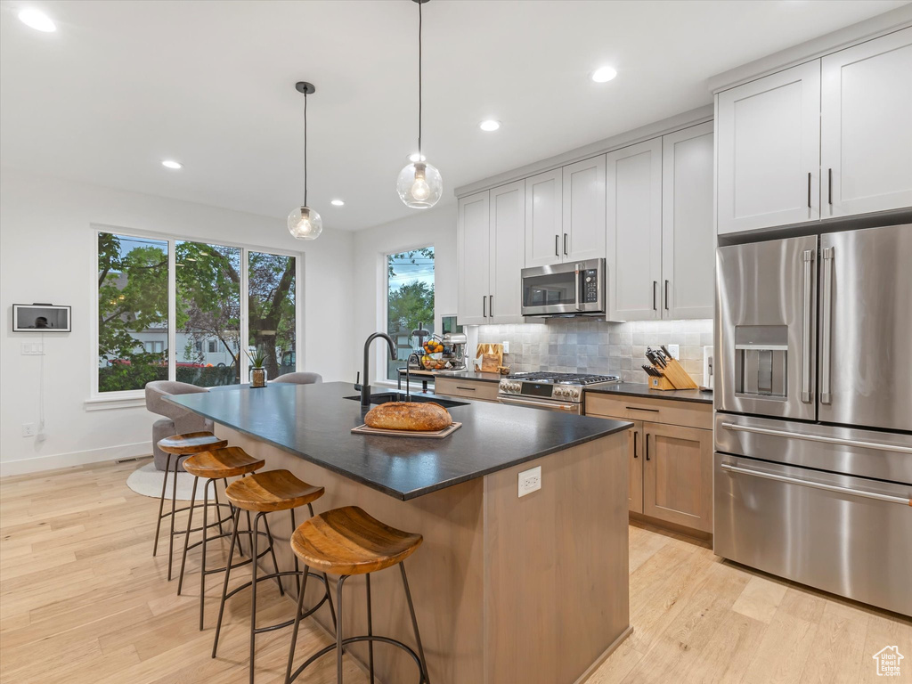 Kitchen with a sink, stainless steel appliances, tasteful backsplash, light wood-type flooring, and dark countertops