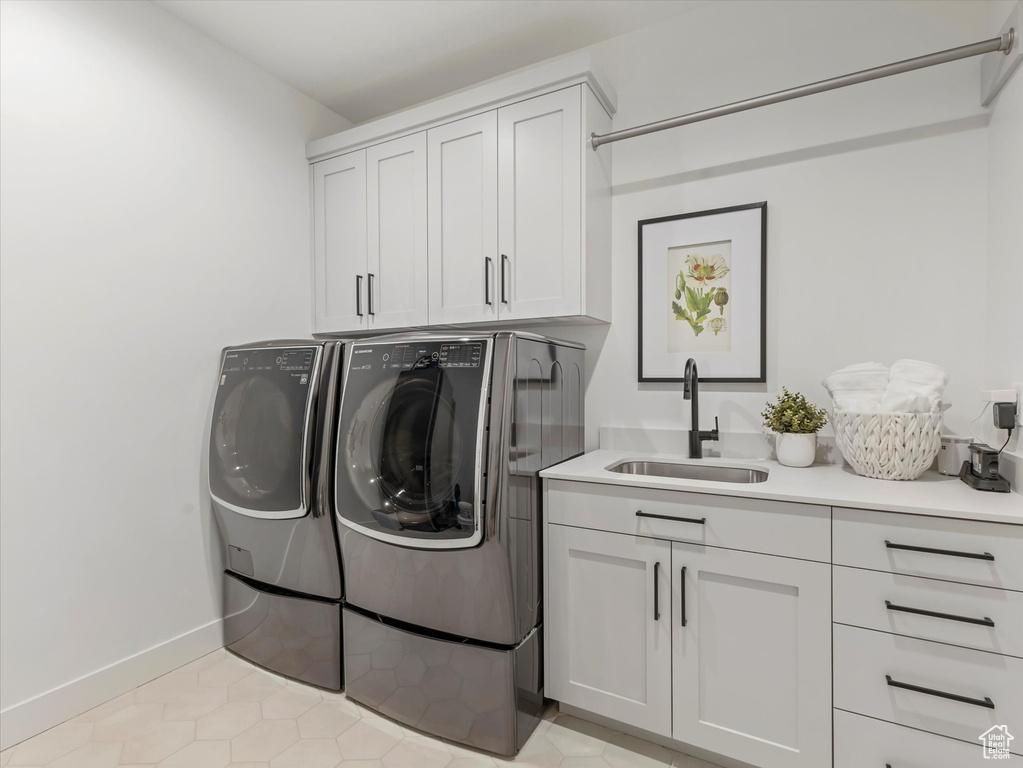 Clothes washing area featuring light tile patterned floors, washer and dryer, cabinet space, a sink, and baseboards