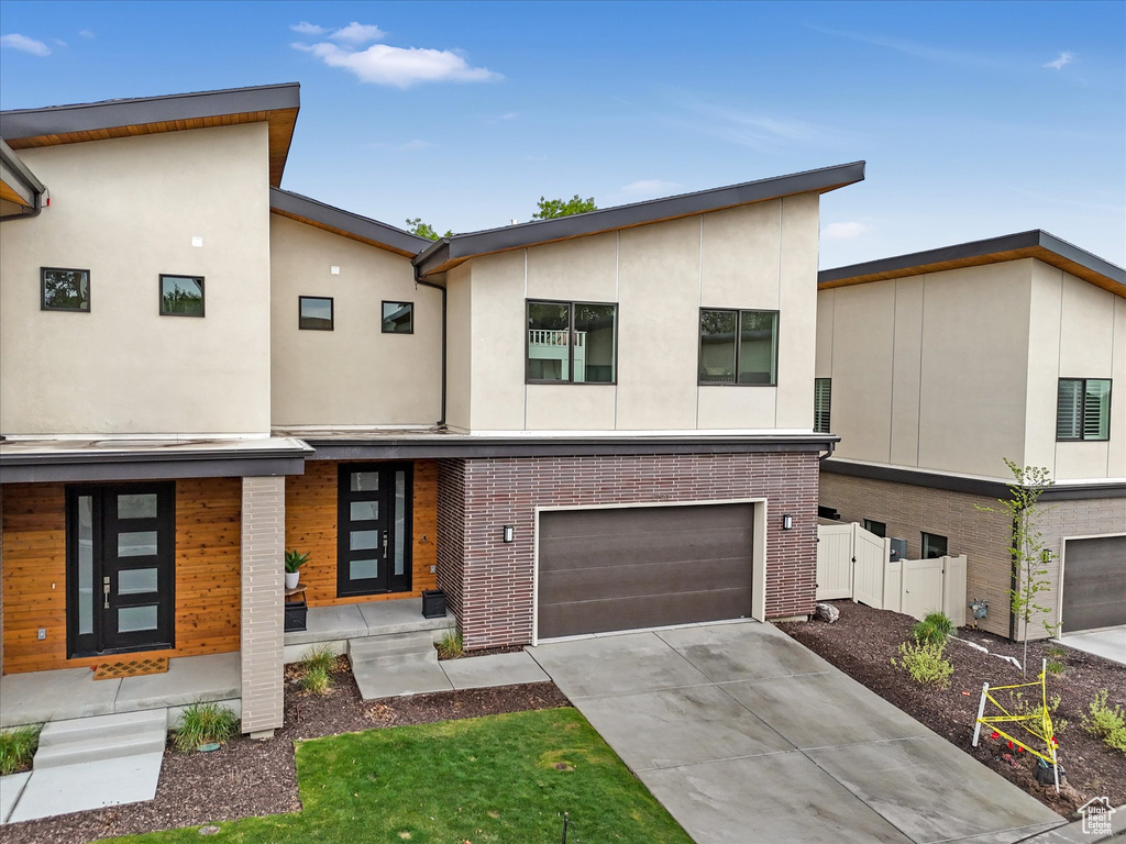 Modern home with stucco siding, brick siding, fence, a garage, and driveway
