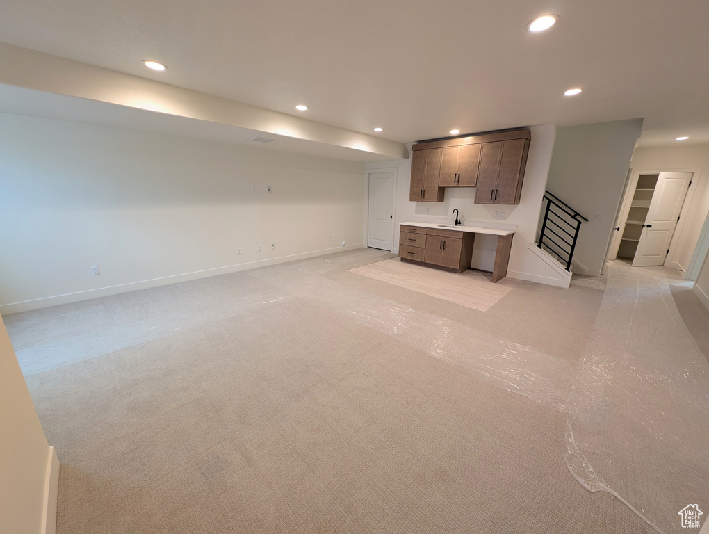 Unfurnished living room featuring a sink, light carpet, wet bar, baseboards, and recessed lighting