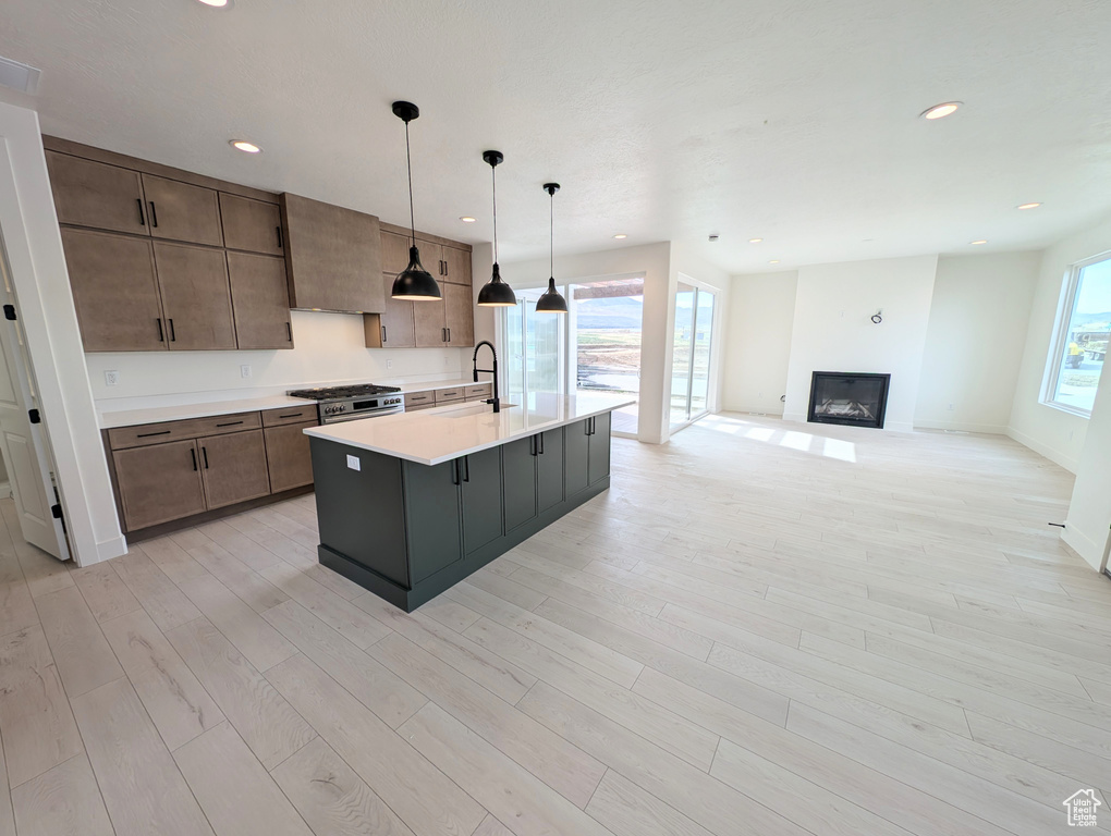 Kitchen with a kitchen island with sink, recessed lighting, light wood-style floors, light countertops, and a fireplace