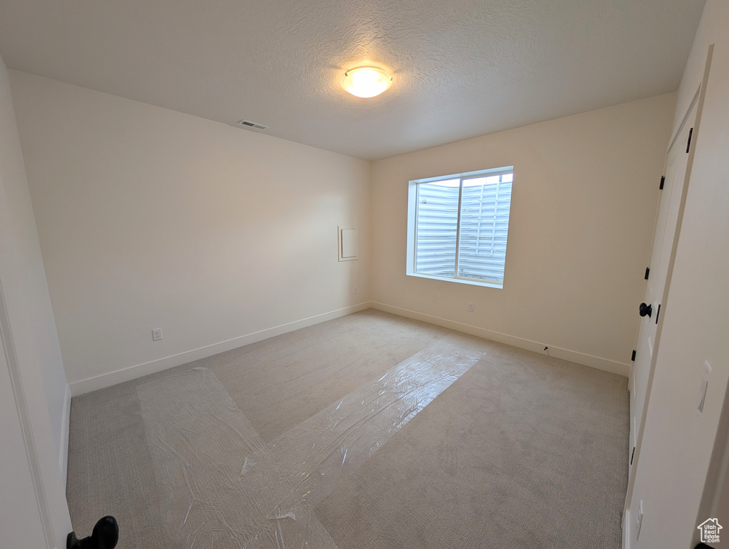 Empty room featuring light colored carpet, baseboards, a textured ceiling, and visible vents