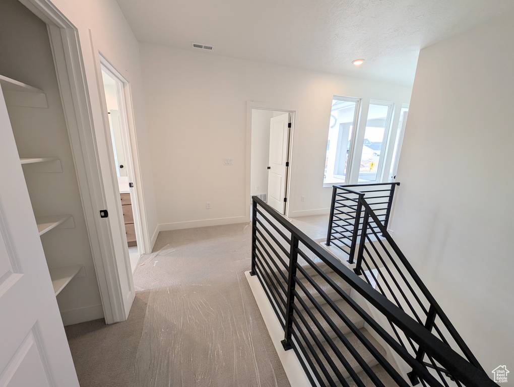 Hallway with baseboards, visible vents, an upstairs landing, and light colored carpet