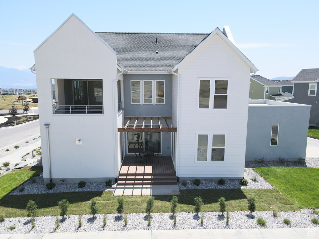 View of front of property featuring a shingled roof, a front yard, a wooden deck, and stucco siding