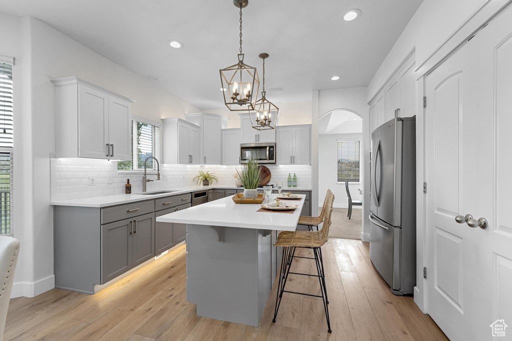 Kitchen featuring gray cabinets, appliances with stainless steel finishes, light countertops, a sink, and a center island