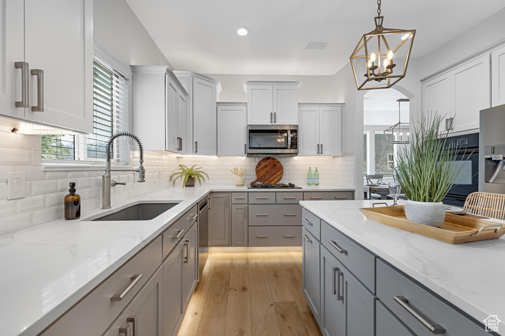 Kitchen featuring gray cabinets, light stone counters, appliances with stainless steel finishes, light wood finished floors, and a sink
