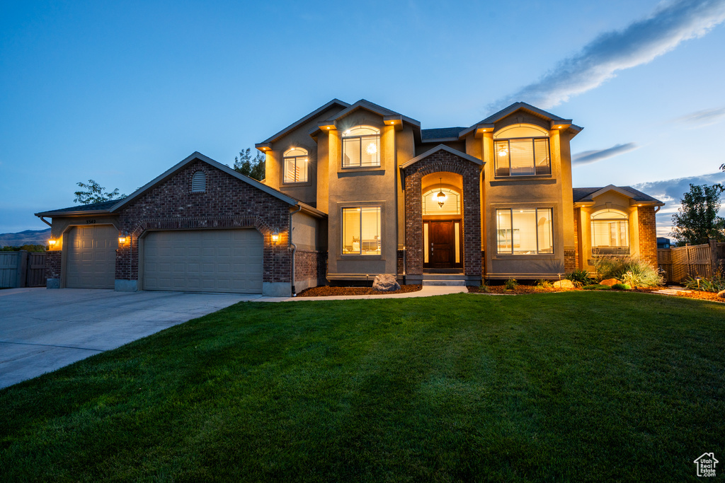 View of front of house featuring a yard, brick siding, fence, a garage, and driveway