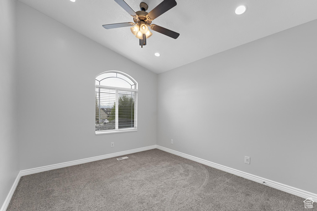 Spare room featuring lofted ceiling, ceiling fan, visible vents, baseboards, and carpet