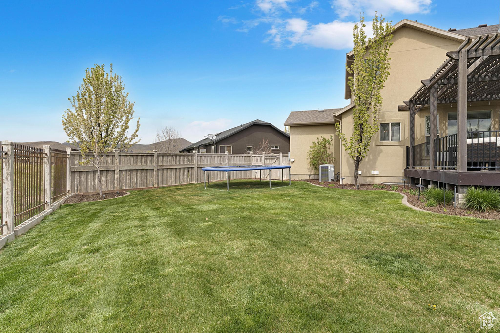 View of yard with a trampoline, a fenced backyard, central AC unit, and a pergola