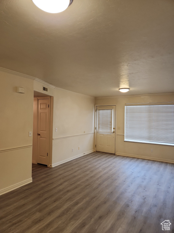 Empty room with baseboards, visible vents, crown molding, and dark wood-style floors