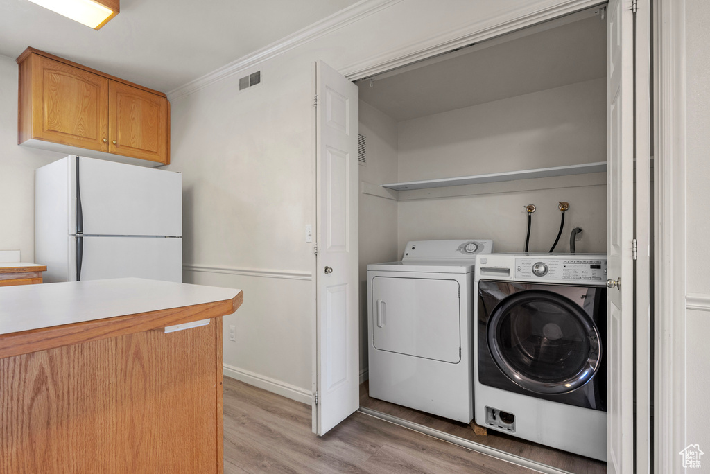 Laundry area with light wood-style floors, separate washer and dryer, and crown molding