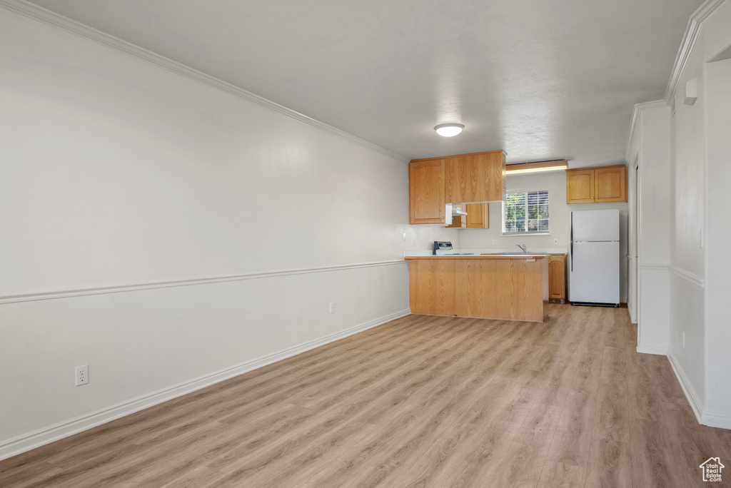 Kitchen with freestanding refrigerator, light wood finished floors, crown molding, a peninsula, and light countertops