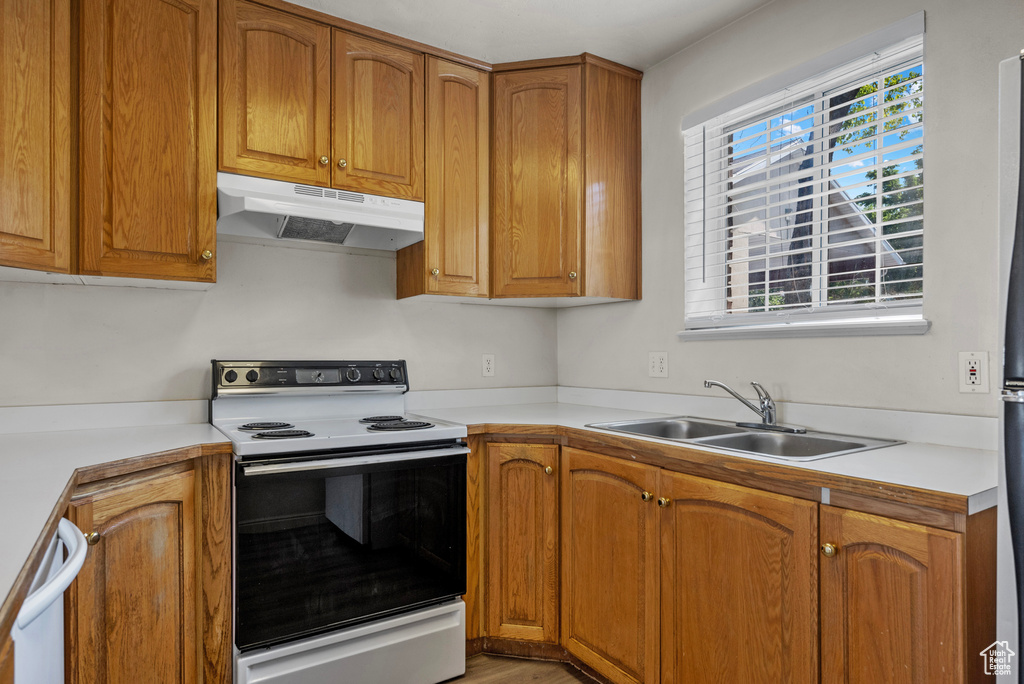 Kitchen featuring white appliances, under cabinet range hood, light countertops, and brown cabinetry