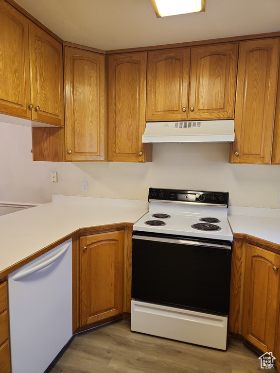 Kitchen with brown cabinetry, under cabinet range hood, white appliances, and light countertops