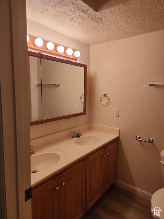 Bathroom with double vanity, wood finished floors, toilet, a sink, and baseboards
