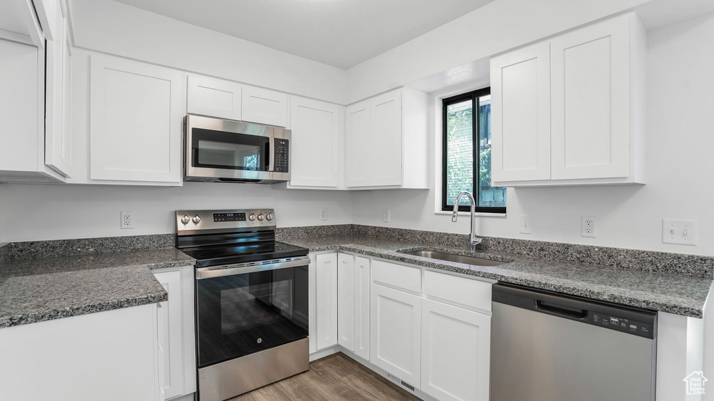 Kitchen featuring appliances with stainless steel finishes, wood finished floors, white cabinetry, and a sink