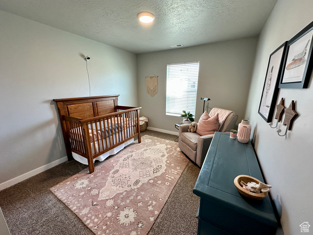 Carpeted bedroom with a crib, visible vents, a textured ceiling, and baseboards