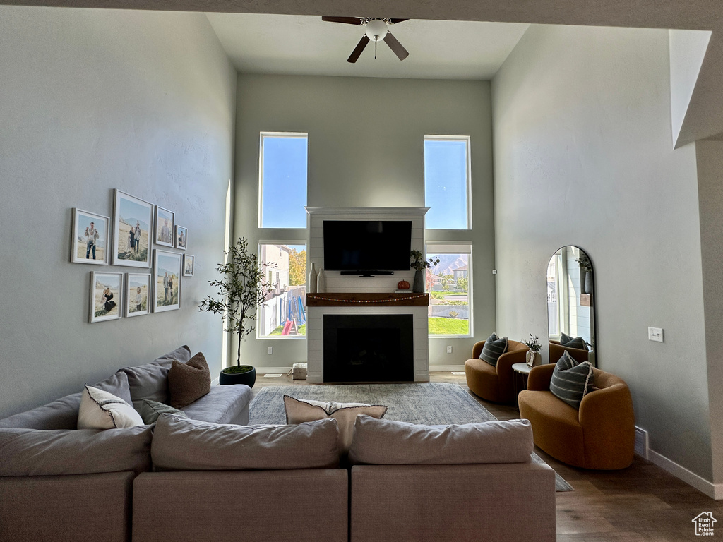 Living area with a towering ceiling, ceiling fan, wood finished floors, and a healthy amount of sunlight