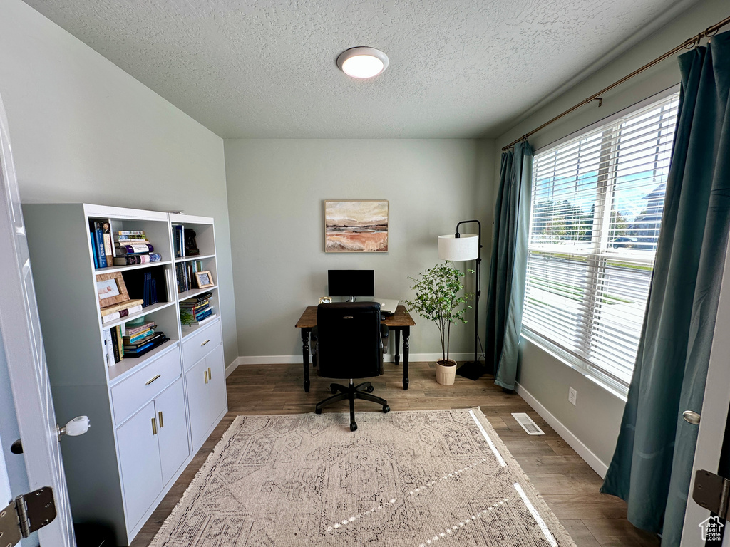Office area with a textured ceiling, visible vents, wood finished floors, and baseboards