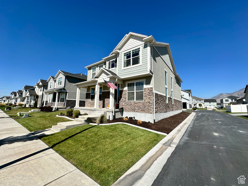 View of front of house featuring a front lawn, a residential view, covered porch, stone siding, and stucco siding