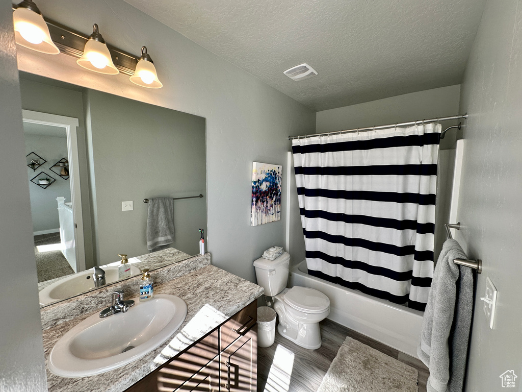 Bathroom with wood finished floors, toilet, vanity, shower / tub combo, and a textured ceiling