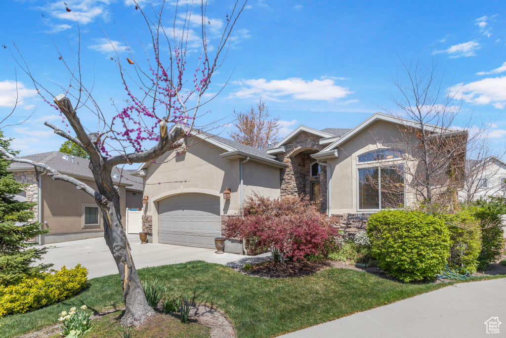 View of front facade featuring an attached garage, stone siding, concrete driveway, and stucco siding