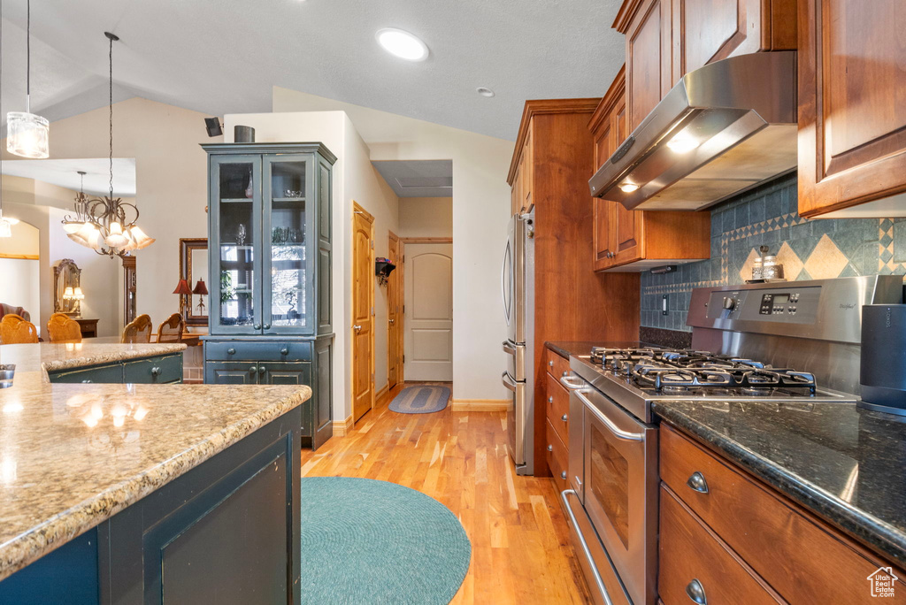 Kitchen with light wood finished floors, dark stone countertops, tasteful backsplash, range hood, and appliances with stainless steel finishes