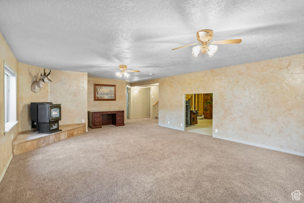 Unfurnished living room featuring carpet, a wood stove, stairs, and ceiling fan