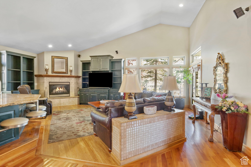 Living room featuring light wood-type flooring, a tile fireplace, recessed lighting, and vaulted ceiling