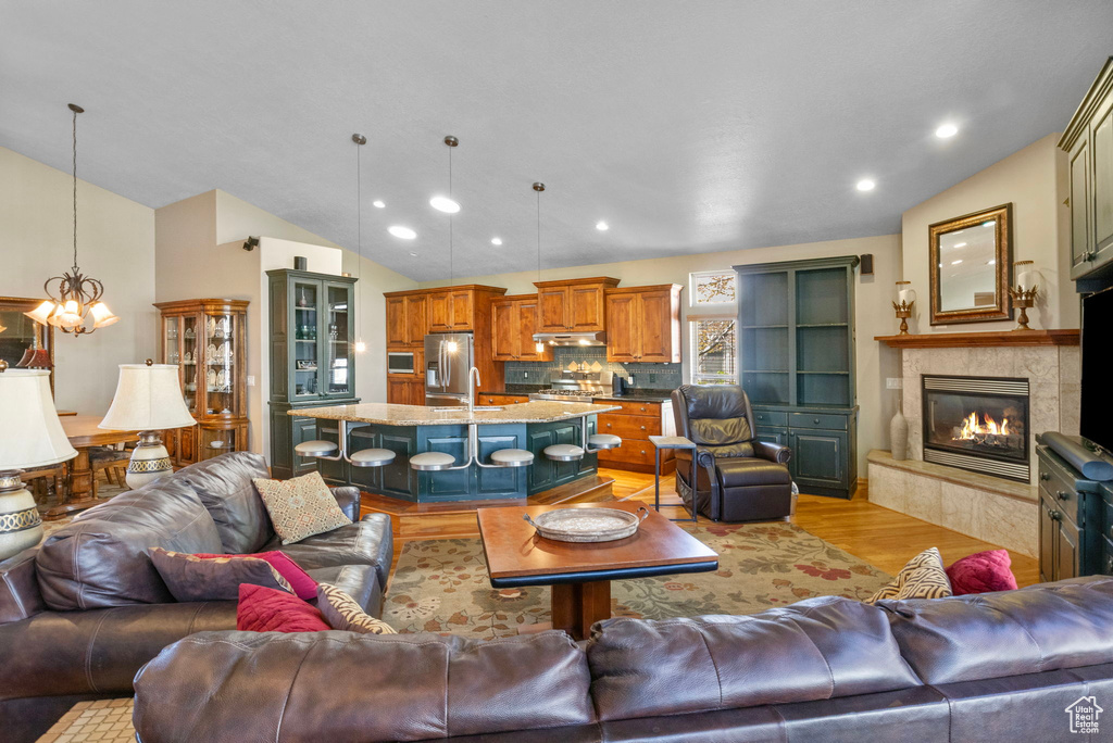 Living area featuring lofted ceiling, an inviting chandelier, a tile fireplace, and light wood finished floors
