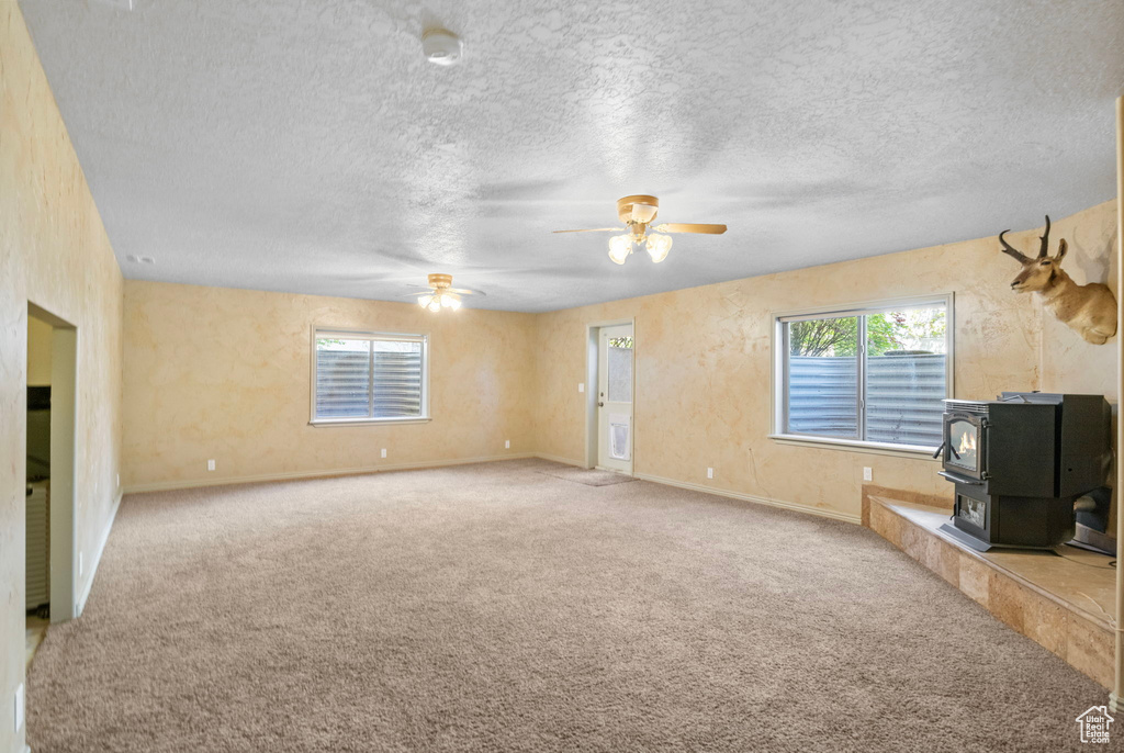 Unfurnished living room featuring carpet floors, a ceiling fan, and a wood stove