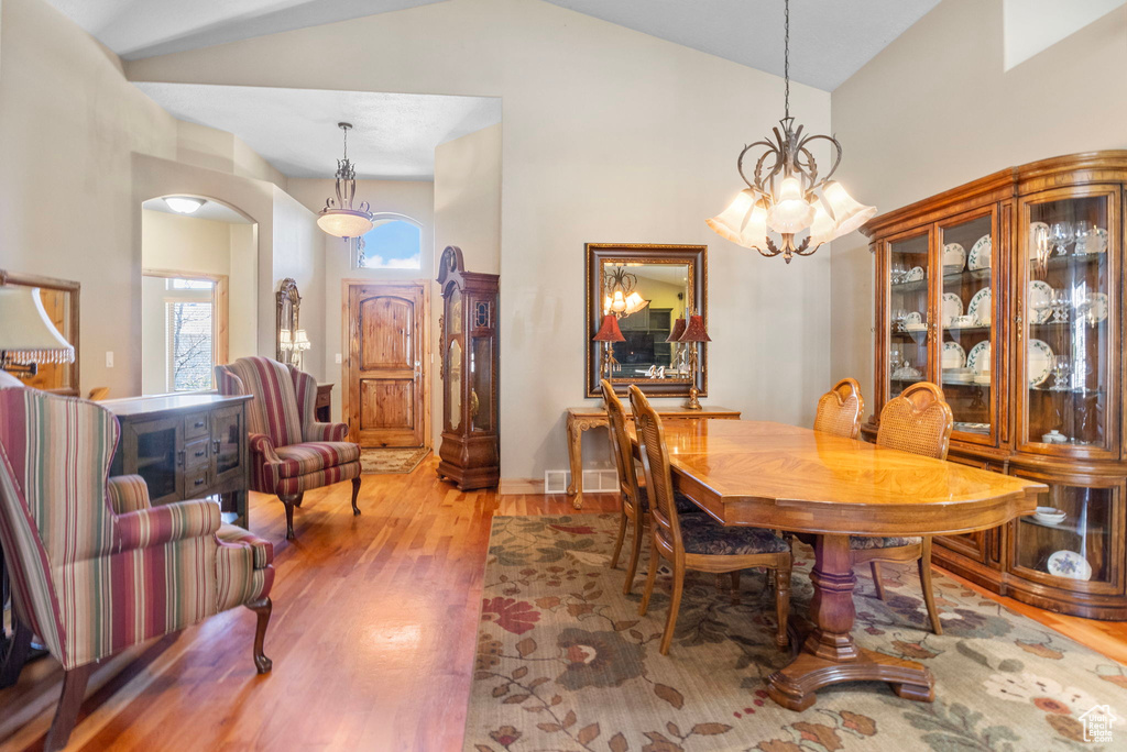 Dining room featuring arched walkways, wood finished floors, high vaulted ceiling, and an inviting chandelier