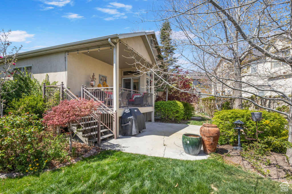 Exterior space featuring stairs, stucco siding, a patio area, a lawn, and a deck