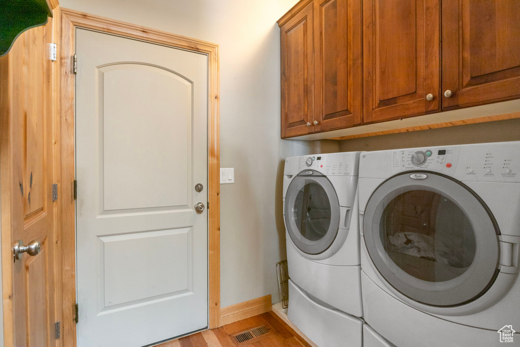 Laundry area with light wood finished floors, visible vents, washing machine and dryer, baseboards, and cabinet space