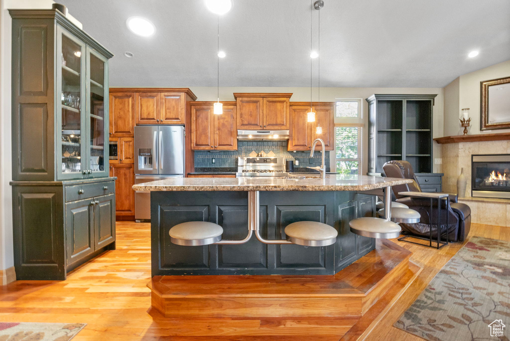 Kitchen with stove, under cabinet range hood, light wood-type flooring, a kitchen bar, and stainless steel refrigerator with ice dispenser