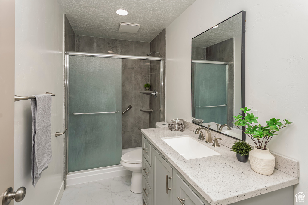 Bathroom featuring a textured ceiling, a stall shower, toilet, vanity, and marble finish floor