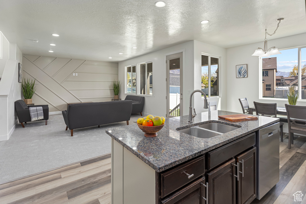 Kitchen with dark stone countertops, stainless steel dishwasher, a center island with sink, and a sink