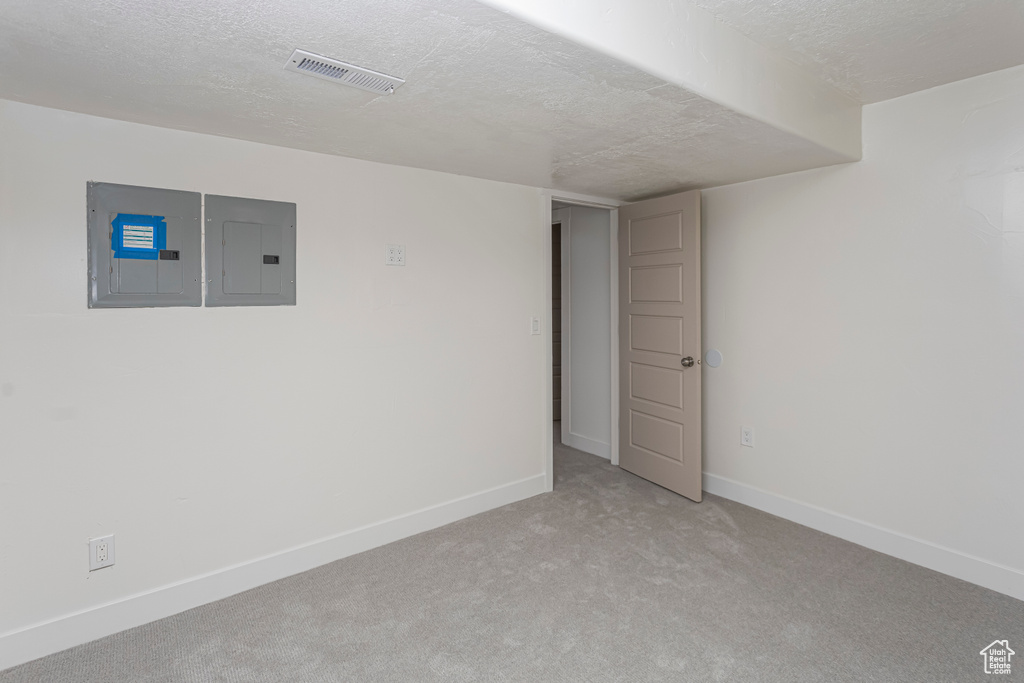 Basement with a textured ceiling, visible vents, electric panel, baseboards, and light carpet